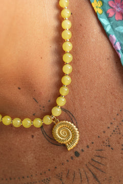 Shop the Ammonite Necklace in Solar Jade Gold, with natural yellow stone beads and a sculpted gold spiral shell pendant from Earth Altering by Jinx the Label.