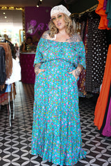 Meet the Dainty Dress in Aqua Bloom, a flowing rayon maxi with an adjustable off-shoulder neckline, elastic waist, tiered skirt and pockets. Handmade in Bali.