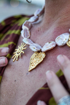 Discover the Sacred Love Necklace in Blush Pearl, featuring irregular freshwater pearls and gold sacred heart, sun and spiral charms by Jinx the Label.
