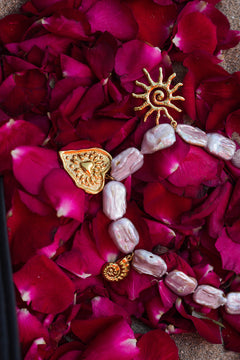 Discover the Sacred Love Necklace in Blush Pearl, featuring irregular freshwater pearls and gold sacred heart, sun and spiral charms by Jinx the Label.