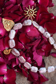 Discover the Sacred Love Necklace in Blush Pearl, featuring irregular freshwater pearls and gold sacred heart, sun and spiral charms by Jinx the Label.