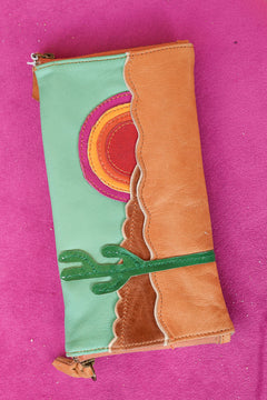Meet the Sundown Sunglass Purse in Caramel, a handcrafted leather sunglass holder featuring a colorful desert sunset and cactus design.