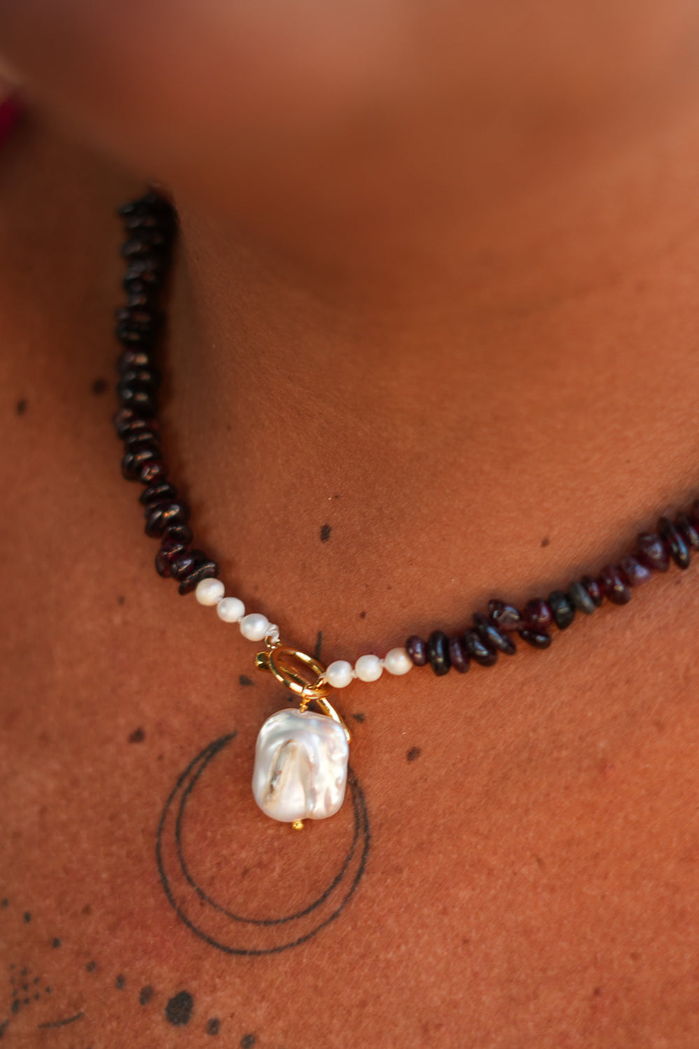 Discover the Wild Heart Necklace in Garnet, featuring deep natural garnet stones, freshwater pearls, a gold toggle and luminous baroque pearl by Jinx the Label.